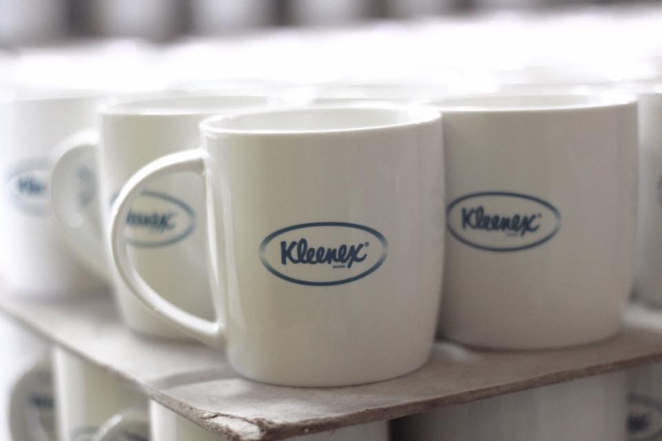 แก้วเซรามิคสีขาวพิมพ์โลโก้ Kleenex เรียงบนชั้นโรงงาน