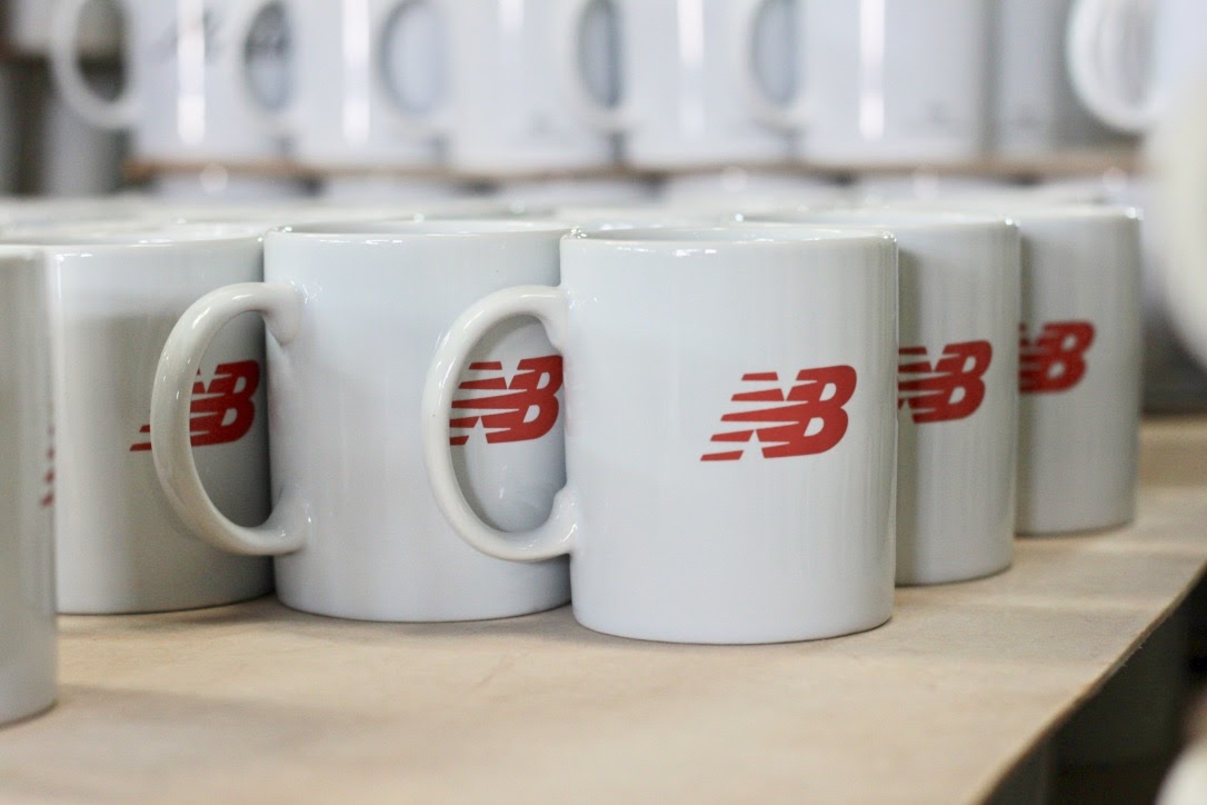 แก้วเซรามิคสีขาวสกรีนโลโก้ New Balance เรียงเป็นชุดในโรงงาน
