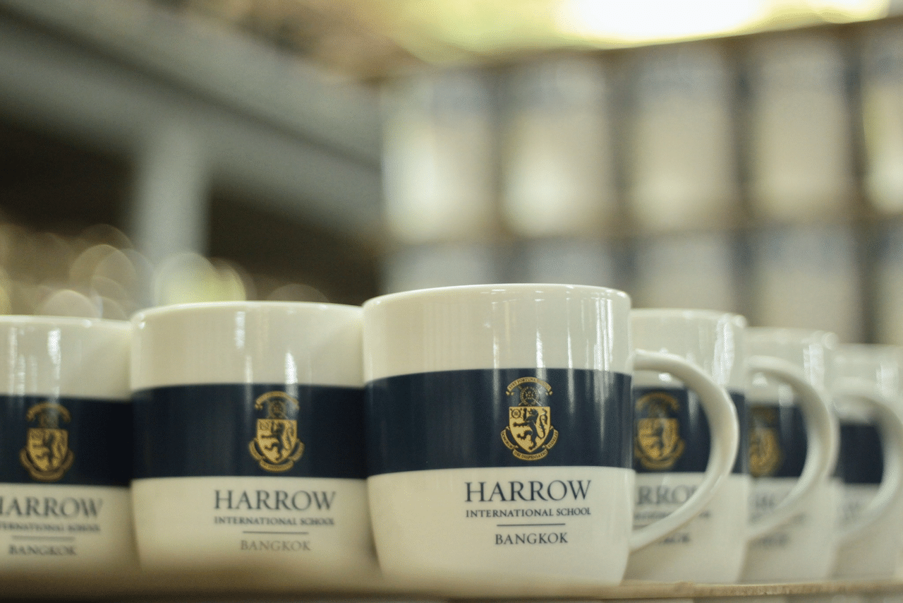 แก้วเซรามิคสีขาวคาดแถบสีน้ำเงินสกรีนโลโก้ Harrow International School